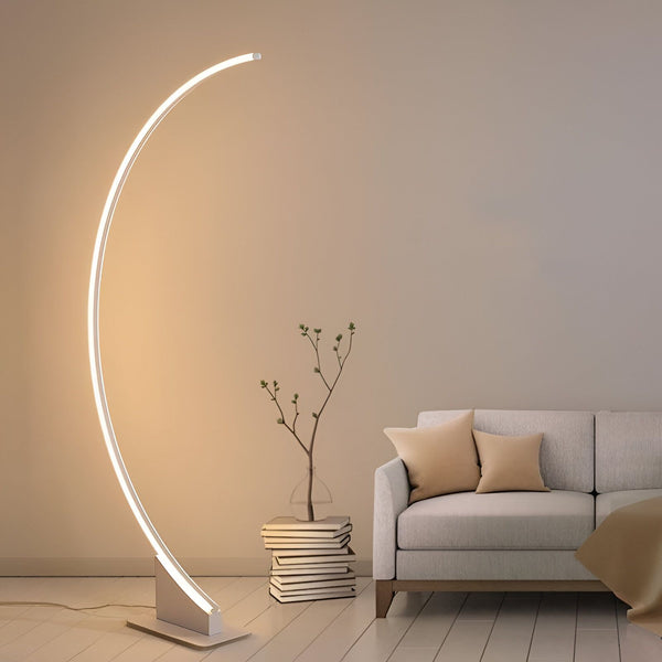 Un lampadaire incurvé blanc est placé à côté d'un canapé gris dans un salon. Il y a une plante verte sur une pile de livres à côté du lampadaire. AR-7946686323,AR-3745116577,