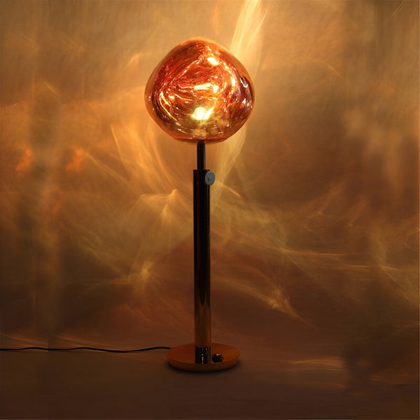 Une lampe en forme de sphère dorée est posée sur un socle doré. La lumière est allumée et se reflète sur la surface de la sphère. LA-1863295534,LA-9235714060,LA-3407836902,