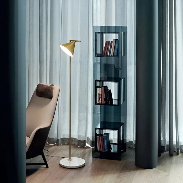 Un lampadaire doré avec un abat-jour blanc est placé à côté d'un fauteuil beige et d'une bibliothèque en verre fumé. Le lampadaire est en acier et marbre, l'abat-jour est en métal. La bibliothèque est composée de 4 étagères en verre fumé et d'une structure en acier doré. SY-5268786555,SY-048073173X,