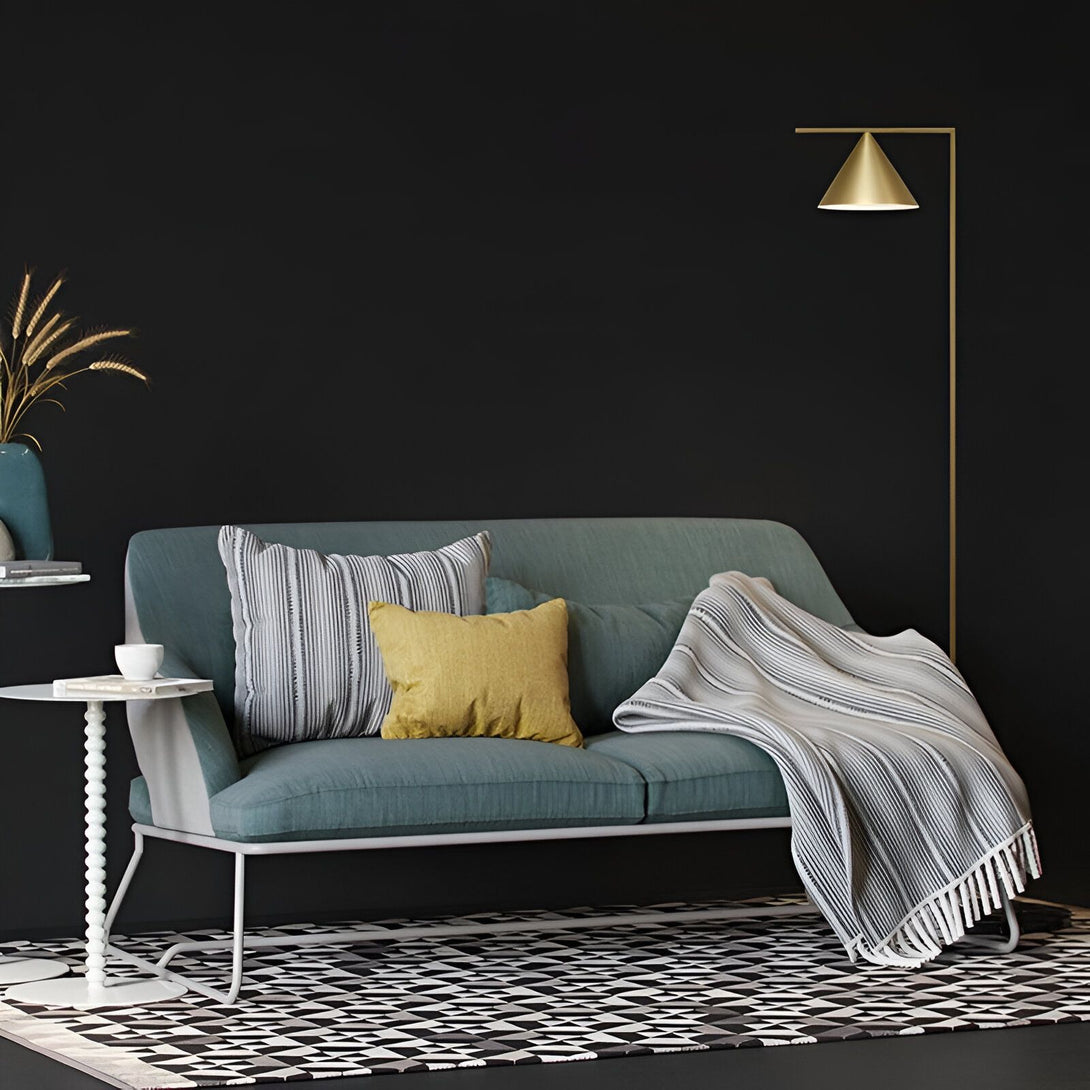 lampadaire sobre en acier et marbre. Il est de couleur laiton et a une forme conique. Il est posé à côté d'un canapé vert et d'une table basse blanche. Il y a un tapis à motifs noir et blanc au sol. SY-5268786555,SY-048073173X,
