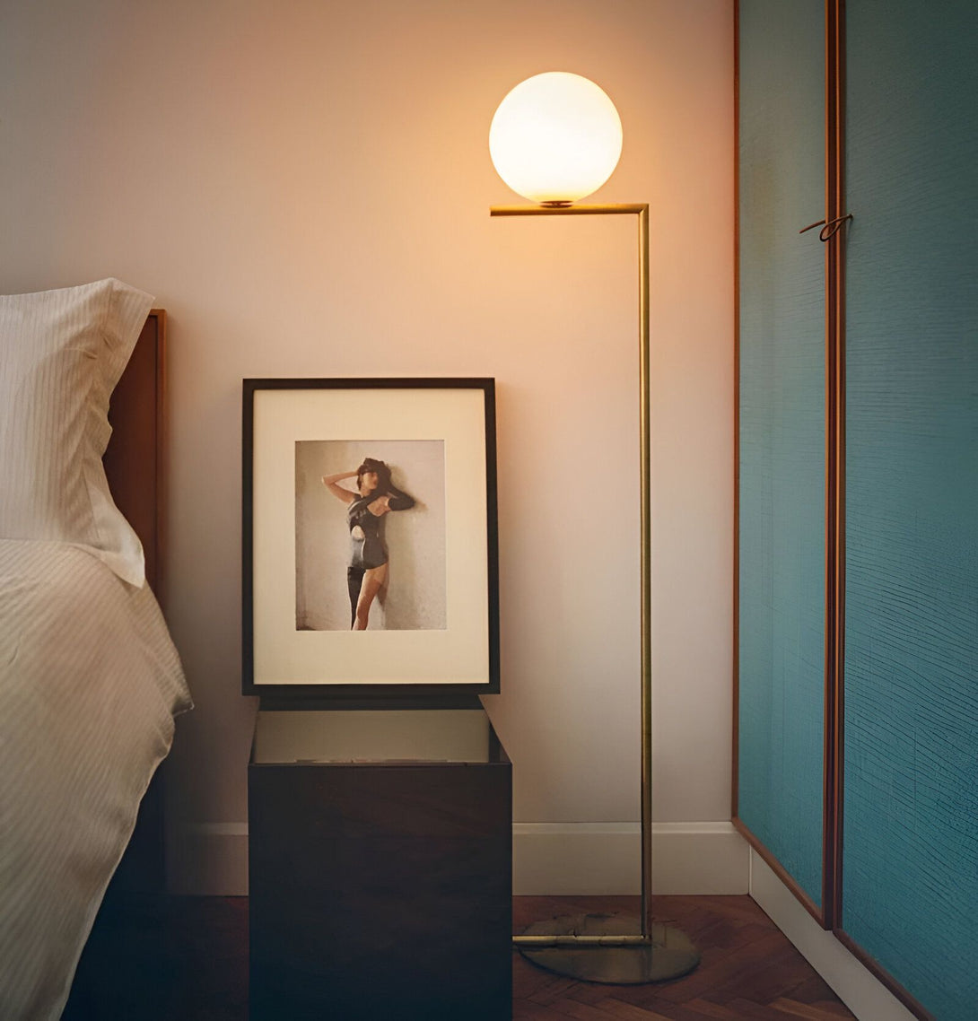 Une image d'une chambre à coucher avec un lit, une table de chevet, une lampe et une armoire. Sur la table de chevet, il y a une photo d'une femme en noir et blanc. La lampe est une grande boule en verre blanc sur un pied en métal doré. L'armoire est bleu turquoise. LS-8060965565,