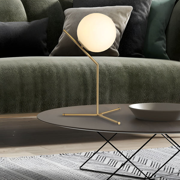 Une lampe de table en métal doré avec un abat-jour en verre blanc est posée sur une table basse noire. CA-2757427814,CA-2757537830,