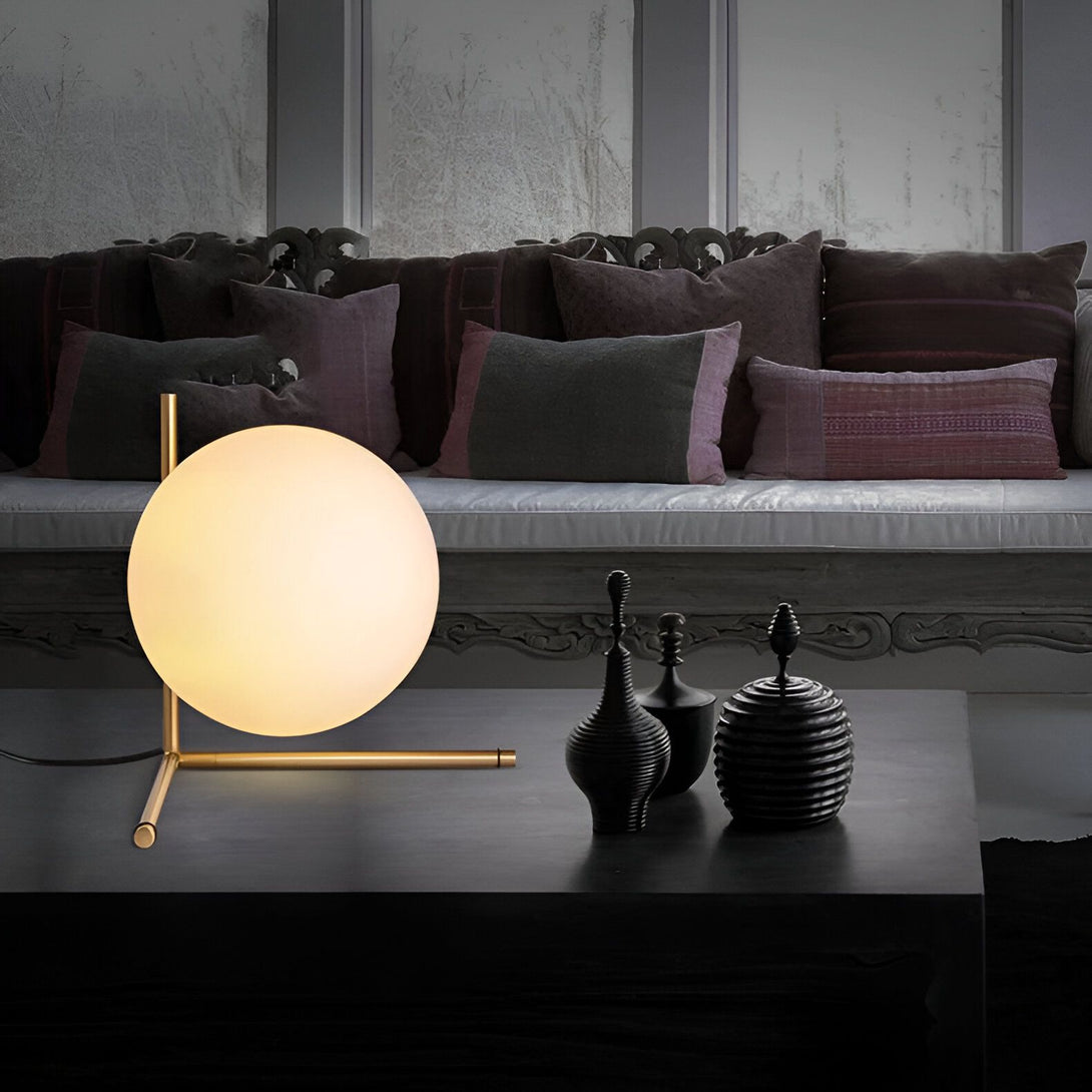 Une lampe sphérique en verre opale est posée sur une table basse noire. À côté, se trouvent trois vases noirs. Derrière la table, se trouve un canapé gris avec des coussins noirs et blancs. CA-2757427814,CA-2757537830,