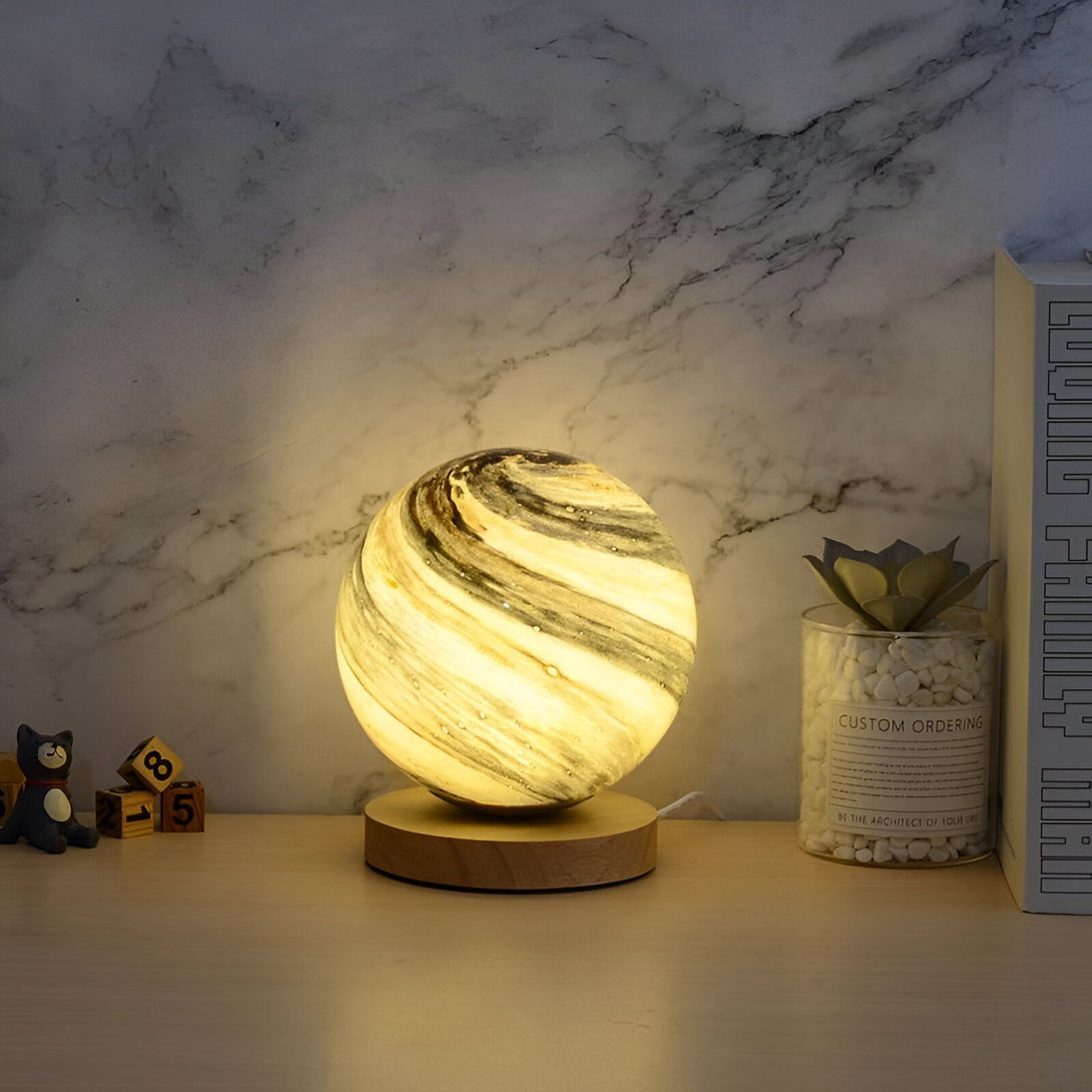 Une lampe en verre soufflé de forme sphérique est posée sur un socle en bois. La lampe est éclairée de l'intérieur et diffuse une lumière douce et tamisée. OR-7630686498,OR-0614193508,