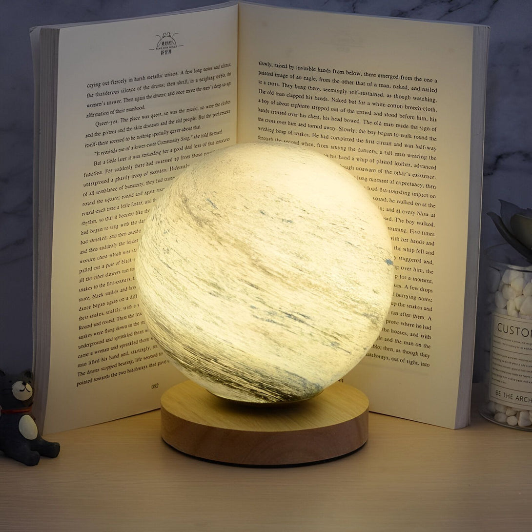 Une lampe en forme de lune en train de briller à côté d'un livre ouvert. OR-7630686498,OR-0614193508,