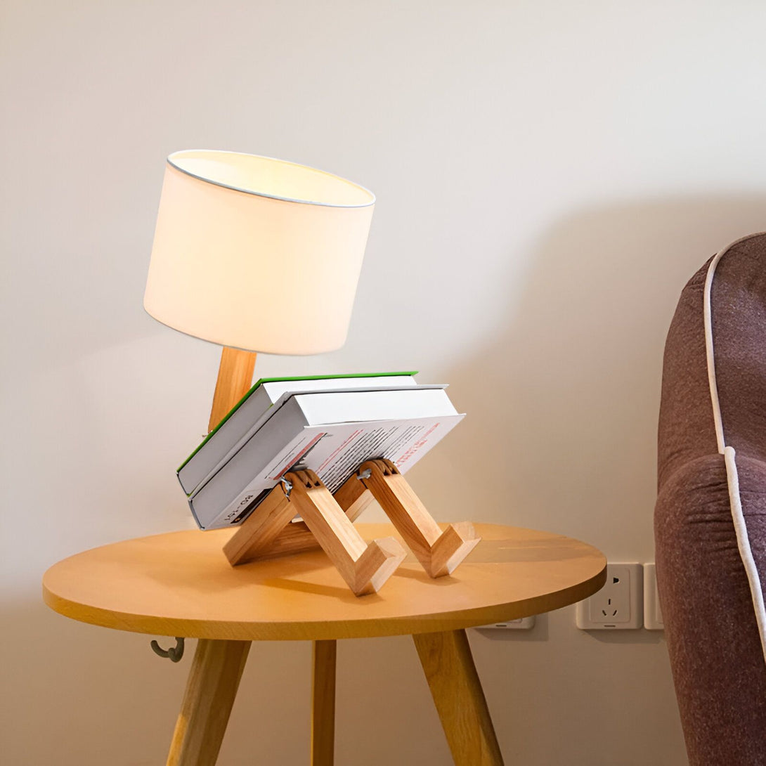 Une lampe de chevet en bois avec un abat-jour blanc est posée sur une table basse en bois. À côté d'elle se trouve un livre ouvert. LY-7887404320,LY-793791999X,