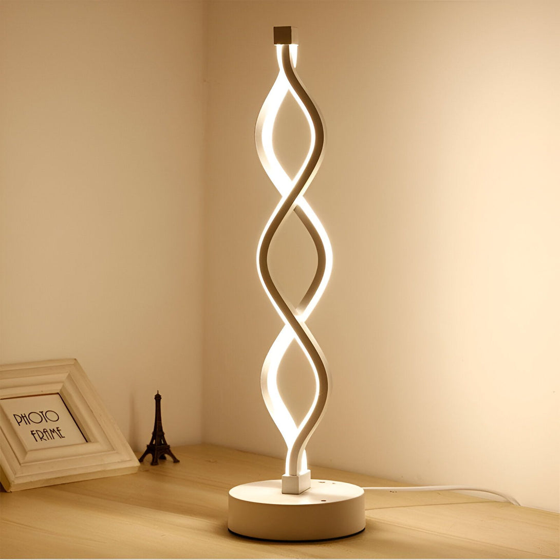 Une lampe de table blanche en forme de spirale. La lampe est posée sur une table en bois. A côté de la lampe, il y a un cadre photo et une tour Eiffel miniature. IN-761638868X,IN-2865725197,IN-8287419824,IN-8037118681,