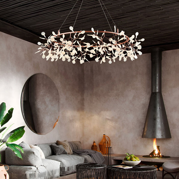 Une image d'un lustre rond en métal avec des branches et des feuilles en verre blanc. Le lustre est suspendu au plafond et il y a un canapé en dessous. Il y a aussi une cheminée et une table basse dans la pièce.