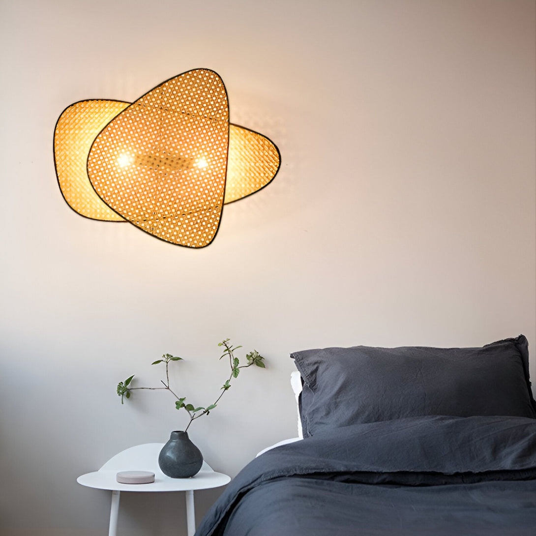 Une applique murale en rotin tressé émettant une lumière tamisée au-dessus d'un lit avec des draps gris. BA-0203883330,BA-3132460699,