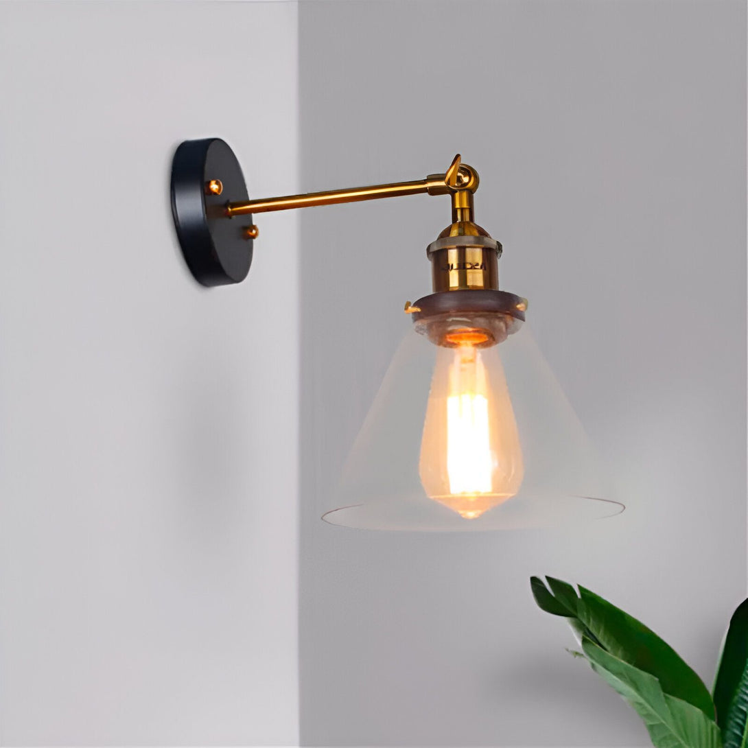 Une image d'une applique murale industrielle. L'applique est en métal noir et doré avec un abat-jour en verre transparent. L'applique est fixée au mur par une plaque ronde en métal noir. L'ampoule est une ampoule à filament. YT-4255477396,YT-8153868179,