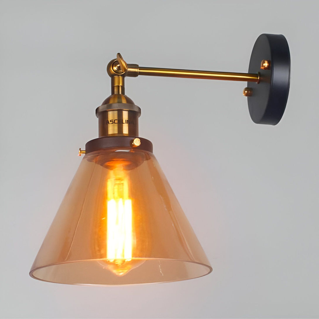Une image d'une applique murale industrielle. L'applique est en métal avec une finition bronze et un abat-jour en verre transparent. L'applique est fixée au mur par une plaque ronde en métal noir. L'ampoule est de couleur ambre. YT-4255477396,YT-8153868179,