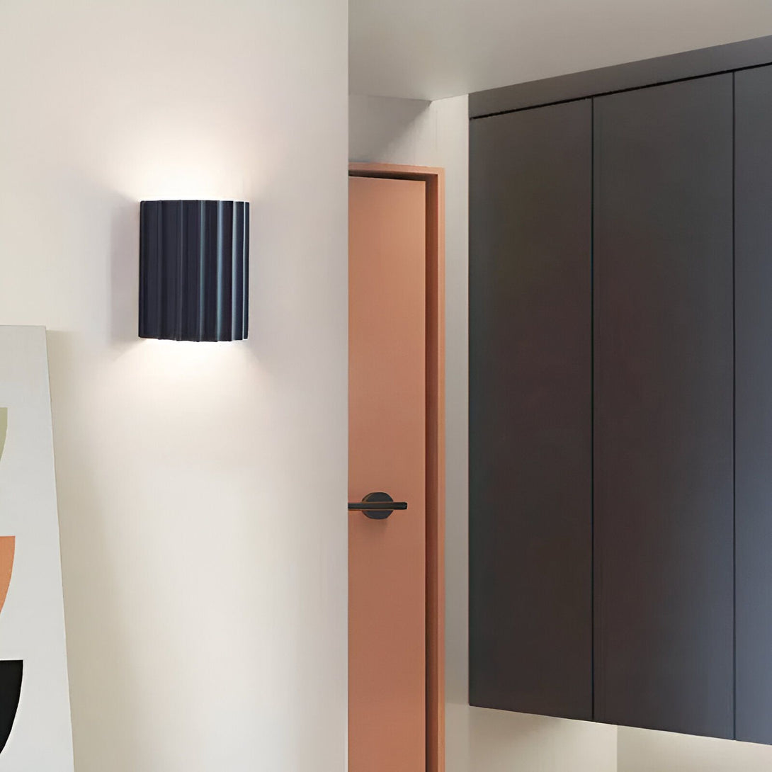 Une image d'une applique murale noire à côté d'une porte peinte en rose. NE-721526775X,NE-8904744822,NE-2805852109,NE-679239677X,