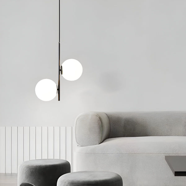 Une image d'un luminaire pour chambre à coucher adulte. Le luminaire est de couleur noire et est composé de deux globes en verre opalin. Il est suspendu au plafond par un fil noir. Le luminaire est allumé et diffuse une lumière douce et tamisée. La chambre à coucher est décorée dans un style moderne et épuré. Les murs sont blancs et le sol est recouvert d'un tapis gris. Le lit est recouvert d'une couette blanche et de deux oreillers gris. Il y a une table de chevet à côté du lit avec une lampe dessus.