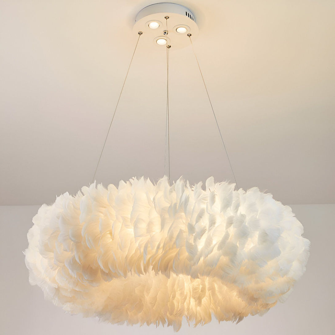 L'image représente un luminaire suspendu en forme de cercle. Il est composé de plumes blanches et est éclairé de l'intérieur. Le luminaire est suspendu au plafond par trois fils fins.