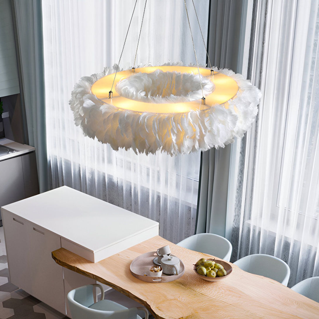 Une suspension en plumes blanches est accrochée au plafond. La suspension est composée d'un cercle en métal blanc et de plumes blanches qui retombent. La suspension est éclairée par une lumière blanche.