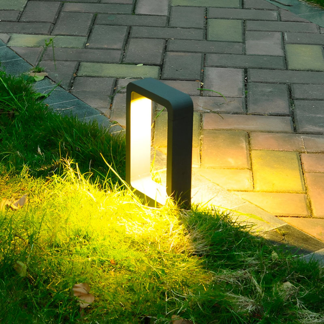 Une image d'une lampe de jardin LED encastrée dans le sol. La lampe est noire et émet une lumière jaune. Elle est installée sur une allée en briques, à côté d'un espace vert. NE-755254144X,NE-2769874705,NE-0294437452,NE-1666104728,NE-5327672107,NE-988439248X,NE-8976410963,NE-906375275X,
