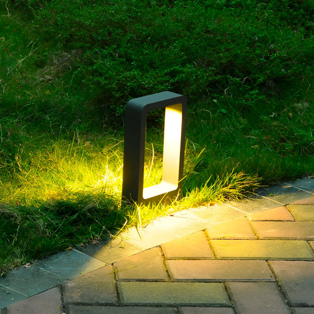 Une image d'une lampe de jardin LED encastrée dans le sol. La lampe est noire et émet une lumière jaune. Elle est installée dans une allée en gravier. NE-755254144X,NE-2769874705,NE-0294437452,NE-1666104728,NE-5327672107,NE-988439248X,NE-8976410963,NE-906375275X,