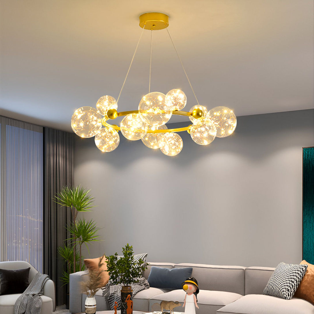 Une image d'un lustre doré avec des boules en verre transparent. Il est suspendu au plafond et il y a un canapé en dessous. BE-1254612327,BE-7357843688,