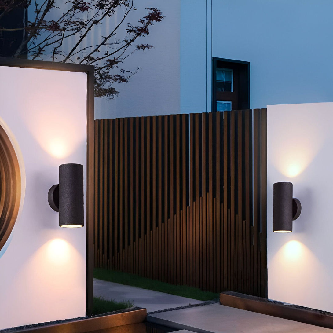Une image d'un luminaire mural extérieur design de la marque Faro Barcelona. Ce luminaire est de couleur noire et possède une forme cylindrique. Il est fabriqué en aluminium et en verre et est équipé d'une ampoule LED. Ce luminaire est idéal pour éclairer une terrasse, un balcon ou une allée. UK-0205687849,UK-2480696774,UK-2510461427,UK-9295319982,UK-3273117745,UK-008158010X,UK-7323325803,UK-3902038195,
