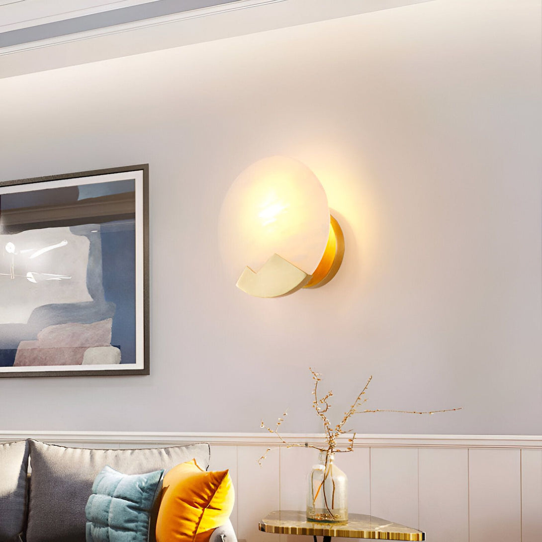 Une applique murale en forme de demi-lune est fixée au mur. Elle est de couleur blanche et dorée. À côté, sur une table, se trouve un vase transparent avec des branches dedans. PA-5944852194,PA-5375841533,