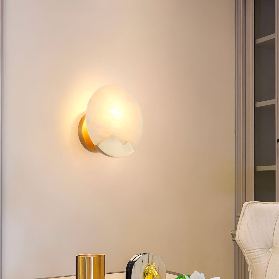 Une applique murale en albâtre et laiton doré. L'albâtre est de forme ronde et le laiton doré est en forme de croissant de lune. L'applique est éclairée par une lumière chaude. PA-5944852194,PA-5375841533,