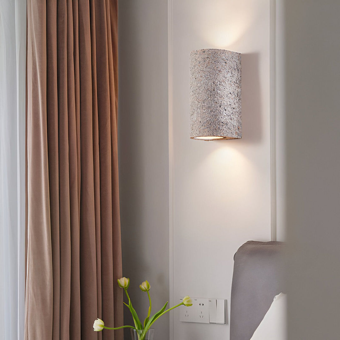 Une applique murale en forme de demi-cylindre en pierre beige est fixée au mur à côté d'un lit. À côté du lit, sur une table de chevet, se trouve un vase avec des tulipes. NA-3923317158,NA-6067964244,NA-3358865746,NA-2876745291,NA-6391241465,
