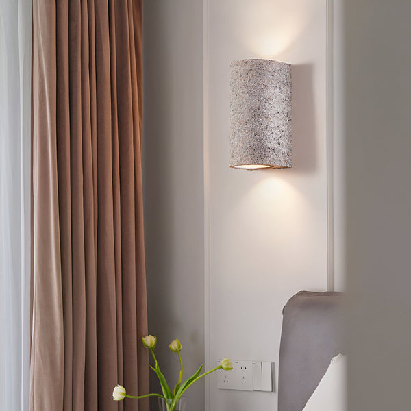 Une applique murale en forme de demi-cylindre en pierre beige est fixée au mur à côté d'un lit. À côté du lit, sur une table de chevet, se trouve un vase avec des tulipes. NA-3923317158,NA-6067964244,NA-3358865746,NA-2876745291,NA-6391241465,