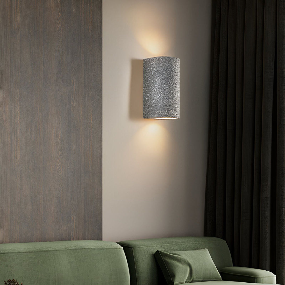 Une applique murale en forme de cylindre texturé gris clair est fixée au mur beige à côté d'un canapé vert. NA-3923317158,NA-6067964244,NA-3358865746,NA-2876745291,NA-6391241465,