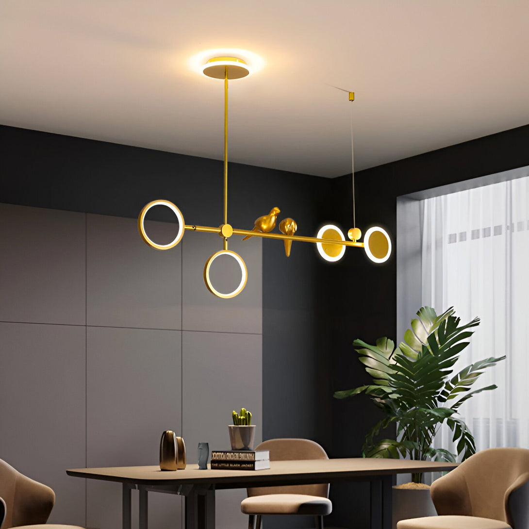 Une image d'un lustre doré avec des oiseaux. Le lustre est composé de trois anneaux et de deux oiseaux. Les anneaux sont de différentes tailles et sont suspendus à des fils dorés. Les oiseaux sont placés sur les anneaux et sont tournés vers le bas. Le lustre est suspendu au plafond par un fil doré. OS-708742372X,OS-509121187X,