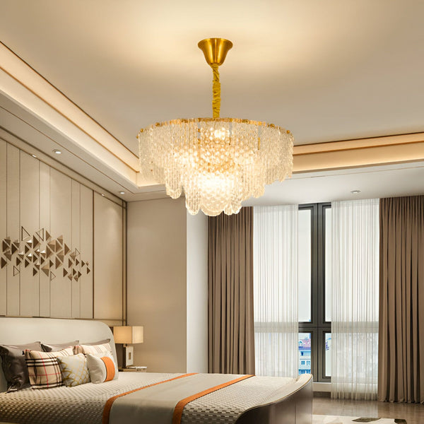 Une image d'un lustre en cristal doré suspendu au plafond d'une chambre à coucher. Le lustre est composé de plusieurs branches en cristal qui s'étendent vers le bas et sont ornées de pampilles en cristal. La chambre à coucher est meublée d'un lit, de deux tables de chevet et d'une armoire. Le lit est recouvert d'une couette et d'oreillers blancs. Les tables de chevet sont en bois et l'armoire est blanche. La chambre est décorée de rideaux blancs et d'un tapis beige.