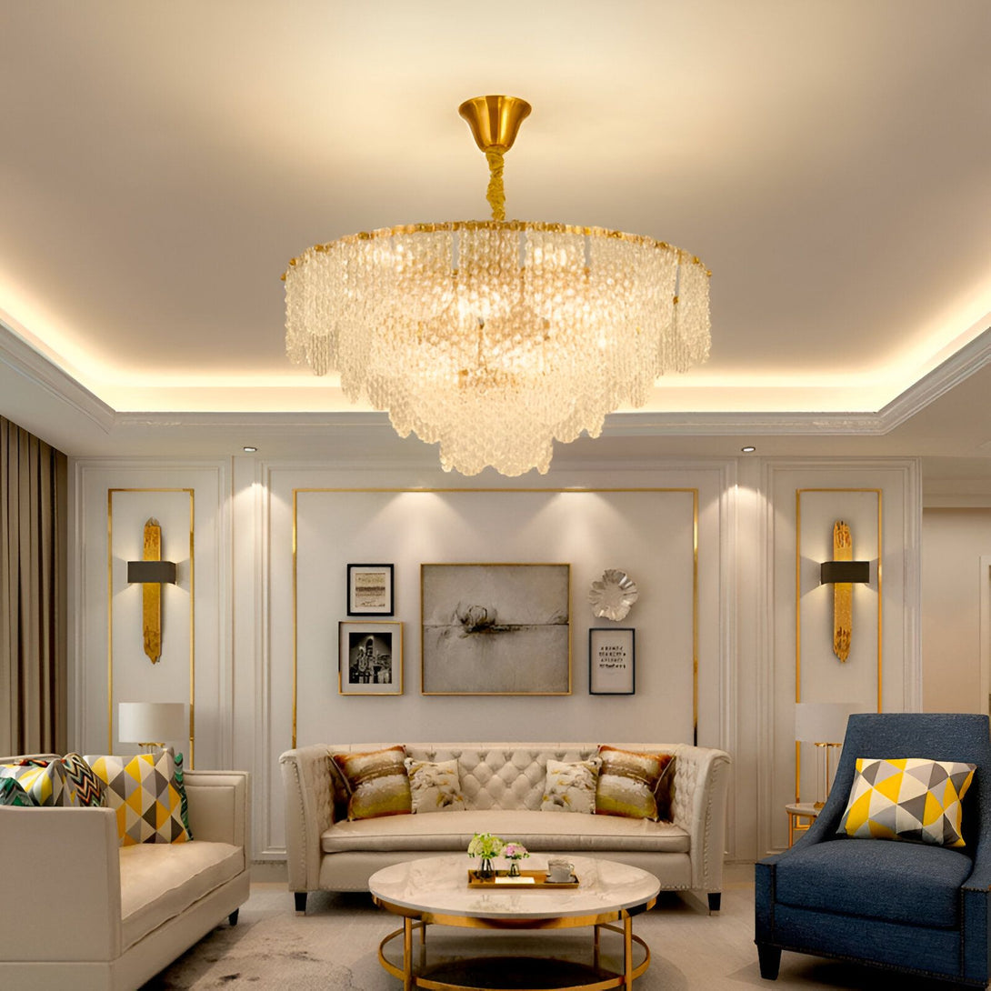 Un lustre doré avec des pampilles en cristal est suspendu au plafond d'un salon. Le lustre est allumé et diffuse une lumière brillante. Le salon est meublé d'un canapé, de fauteuils et d'une table basse. Les murs sont décorés de cadres. PE-8989591325,PE-642660481X,PE-3701985286,PE-234610650X,PE-4491396426,PE-9917021671,