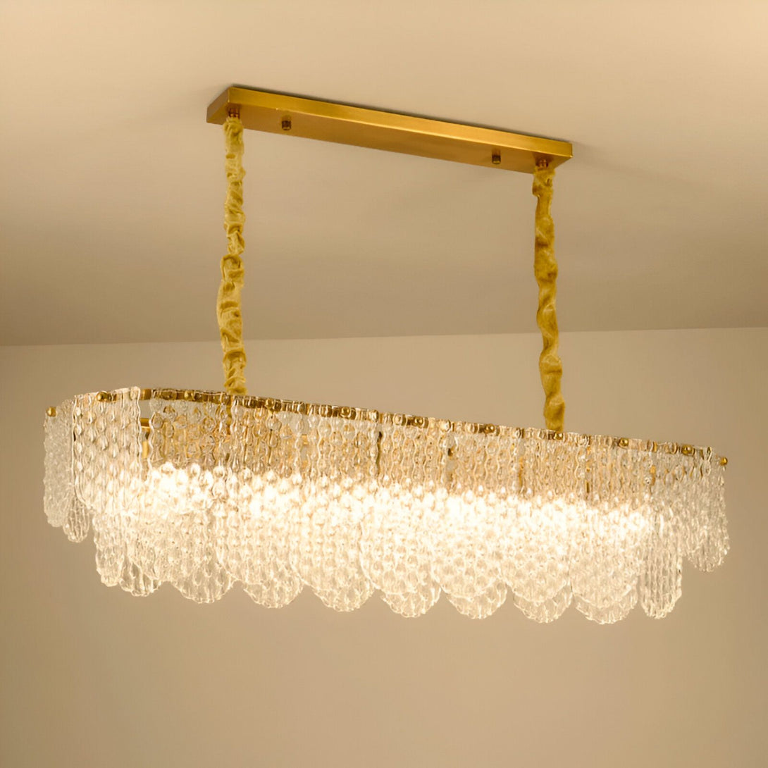 Un lustre rectangulaire en cristal avec une structure en métal doré. Il est suspendu au plafond par deux câbles enroulés de tissu doré. Le lustre est composé de plusieurs rangées de pampilles en cristal transparent. PE-8989591325,PE-642660481X,PE-3701985286,PE-234610650X,PE-4491396426,PE-9917021671,