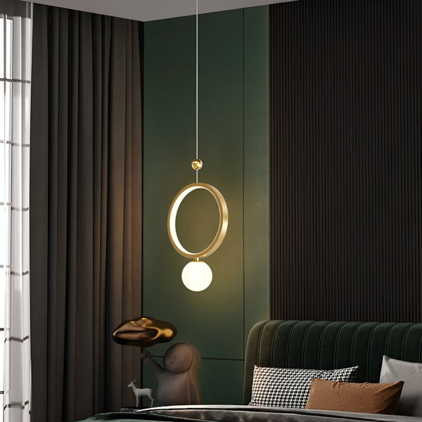 Une image d'une suspension en métal doré avec une sphère en verre opalin. Le luminaire est suspendu par un fil électrique noir. En arrière plan, on aperçoit un mur vert foncé et des rideaux marron. PA-3579302264,