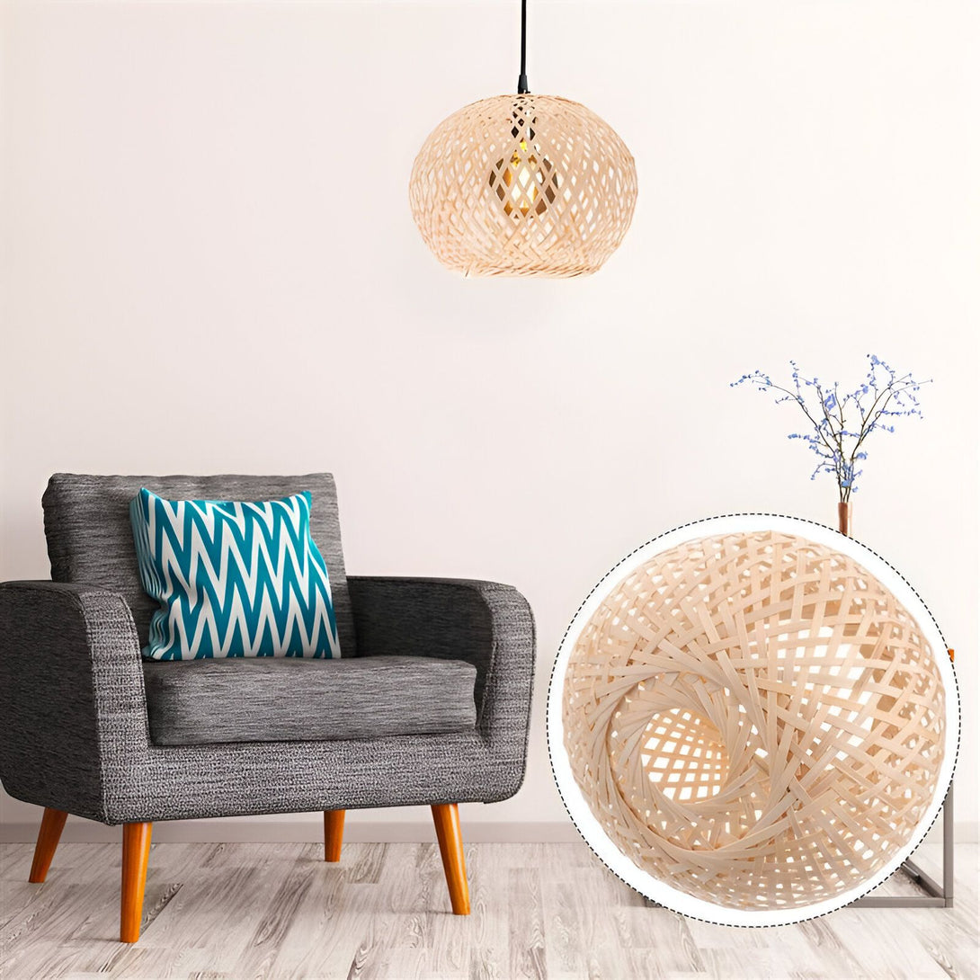 Une lampe en osier suspendue au plafond. La lampe est de forme sphérique et est faite de tiges de bambou tressées. Elle est suspendue par un fil noir. À côté de la lampe, il y a un fauteuil gris avec un coussin bleu et blanc. PA-6497010653,