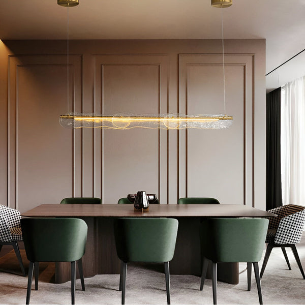 Une vue d'une salle à manger avec une table en bois et des chaises vertes. Il y a un lustre en verre design au-dessus de la table. Le lustre est de forme rectangulaire et est fait de verre transparent. Il y a des ampoules à l'intérieur du lustre qui émettent une lumière chaude. VE-152859987X,VE-1786463202,VE-6110644315,