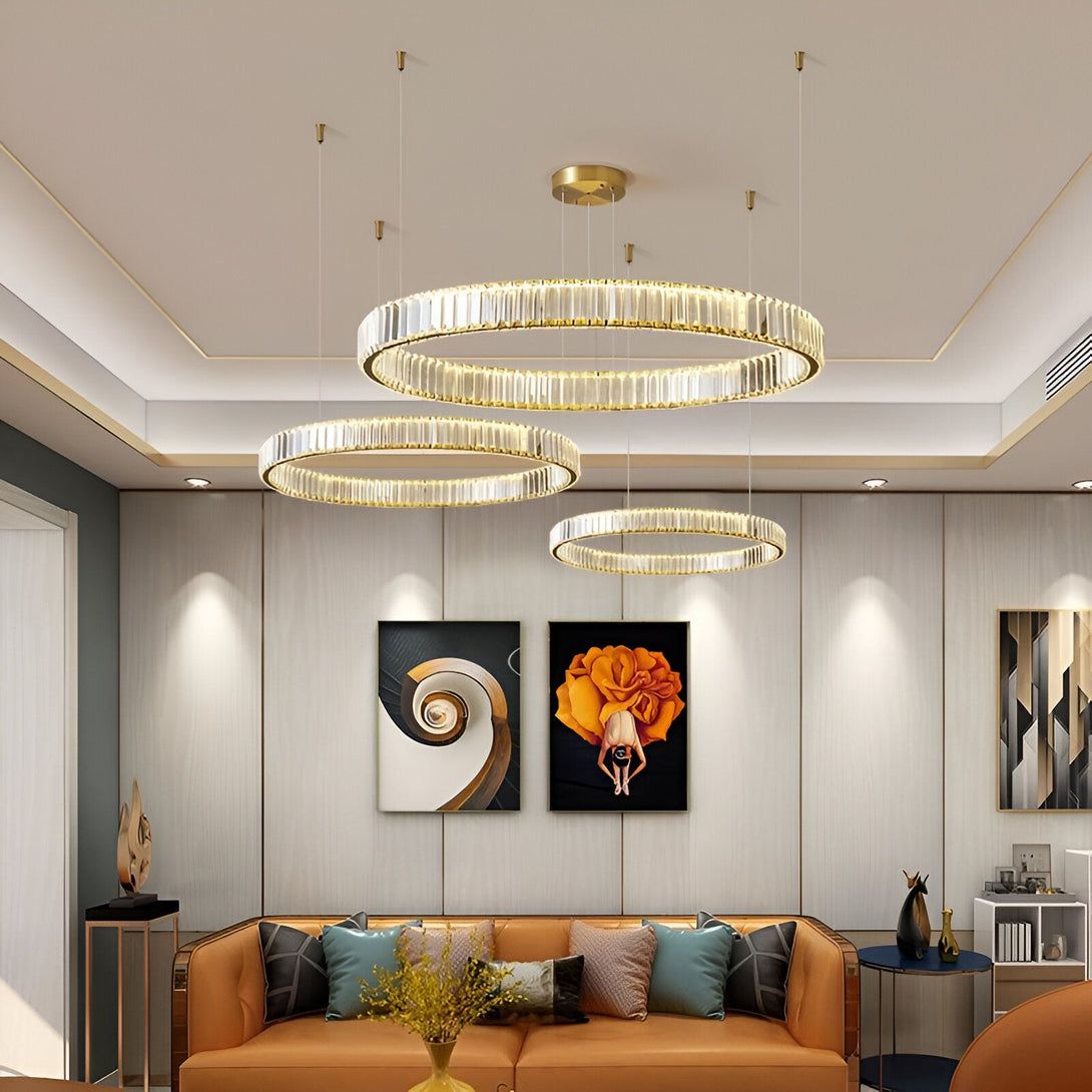 Une image d'un salon avec un lustre rond en cristal doré à LED. Le lustre est suspendu au plafond et est composé de plusieurs anneaux de cristal. Il y a un canapé marron en dessous et des tableaux accrochés au mur. AN-0509298699,AN-2472112572,AN-9517541910,AN-0342778935,