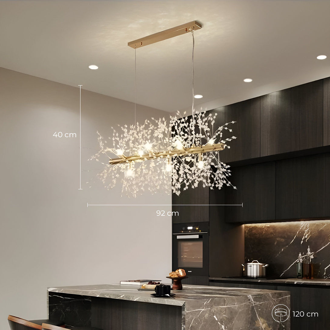 Une image d'un lustre doré suspendu au plafond. Le lustre est composé de plusieurs branches de cristal qui s'étendent vers le bas. Il est allumé et diffuse une lumière brillante. Le lustre est suspendu au-dessus d'un îlot de cuisine avec des tabourets. KH-4176785551,KH-0922345929,