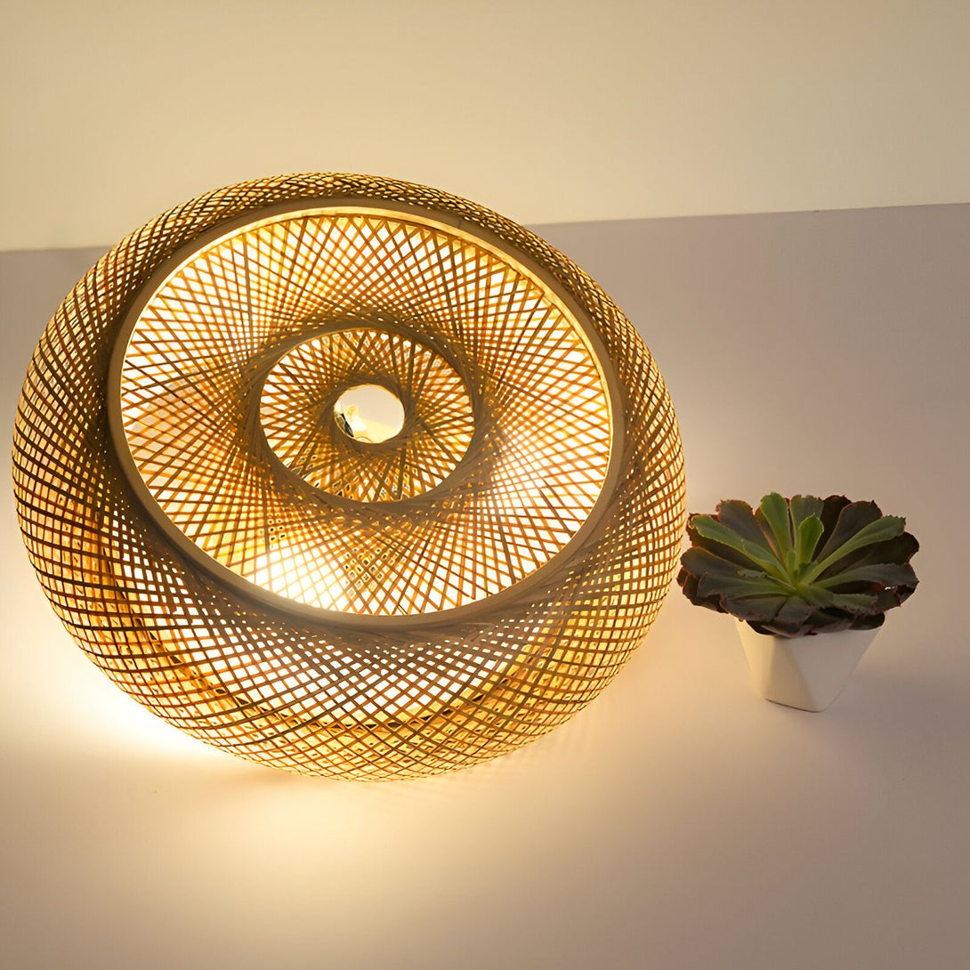 Une lampe en bambou tissé à la main avec une lumière chaude et diffuse. À côté de la lampe, sur la droite, se trouve une plante verte dans un pot blanc. CE-7088600102,CE-8831059041,CE-585684436X,CE-6560594998,