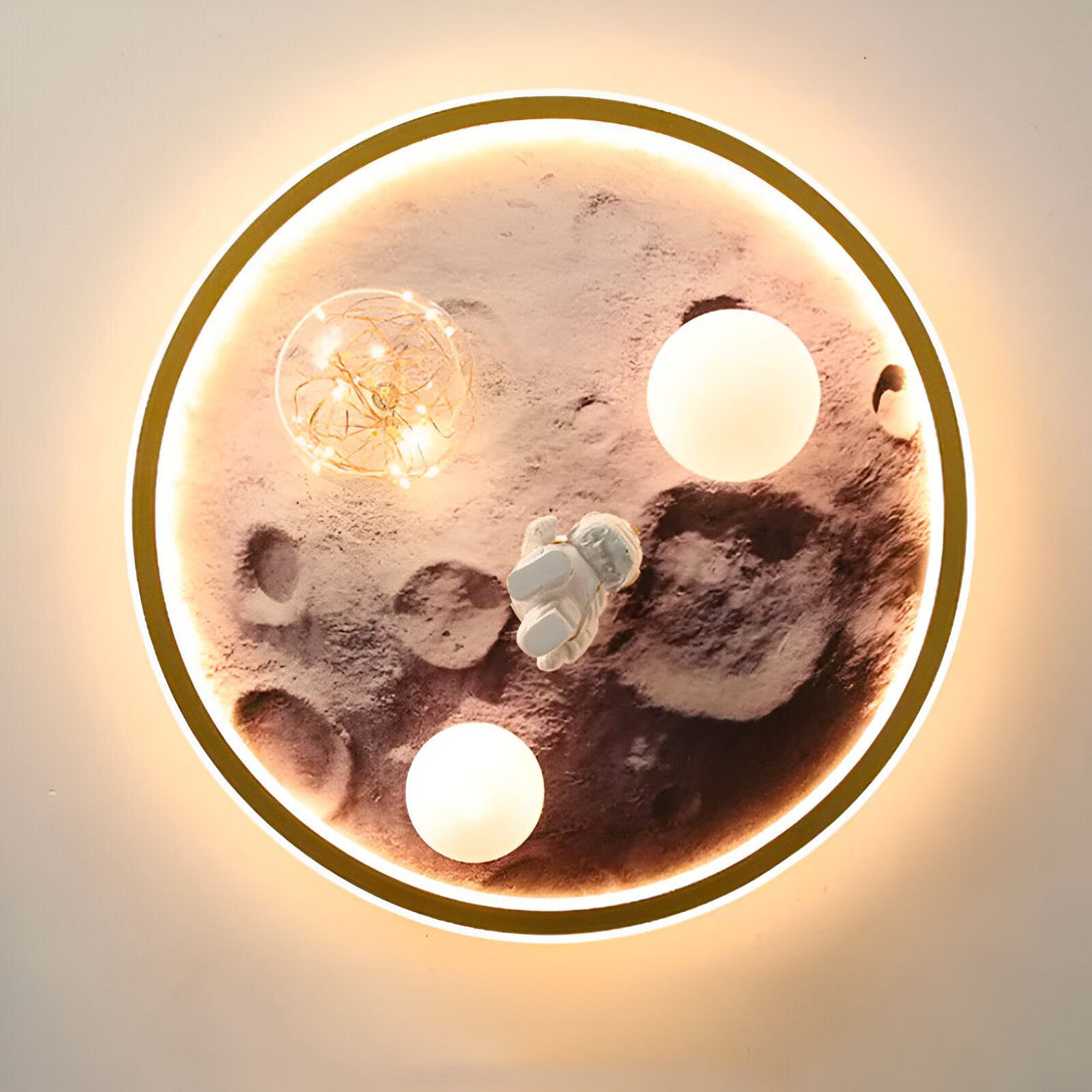 L'image représente une applique murale en forme de lune. La lune est en résine avec un cadre doré. Elle est éclairée par des LED et l'astronaute est en résine blanche. AS-8979596499,