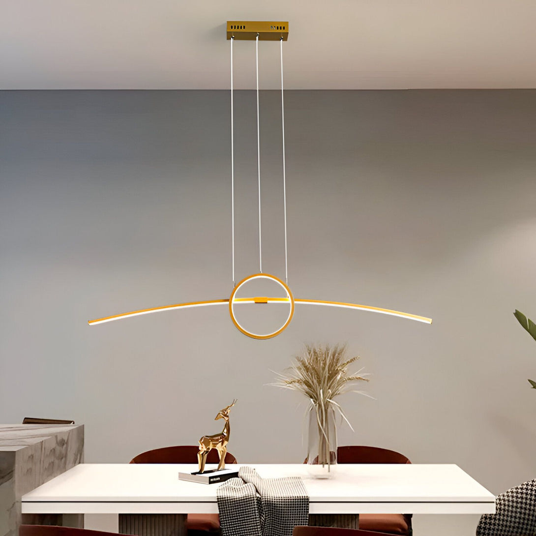 Une image d'une suspension LED en forme d'arc avec un cercle au milieu. La suspension est de couleur dorée et est suspendue au plafond par trois câbles fins. La suspension est allumée et émet une lumière blanche chaude. En dessous se trouve une table à manger en bois avec des chaises et un vase avec des fleurs. LO-6297965579,LO-5510735155,