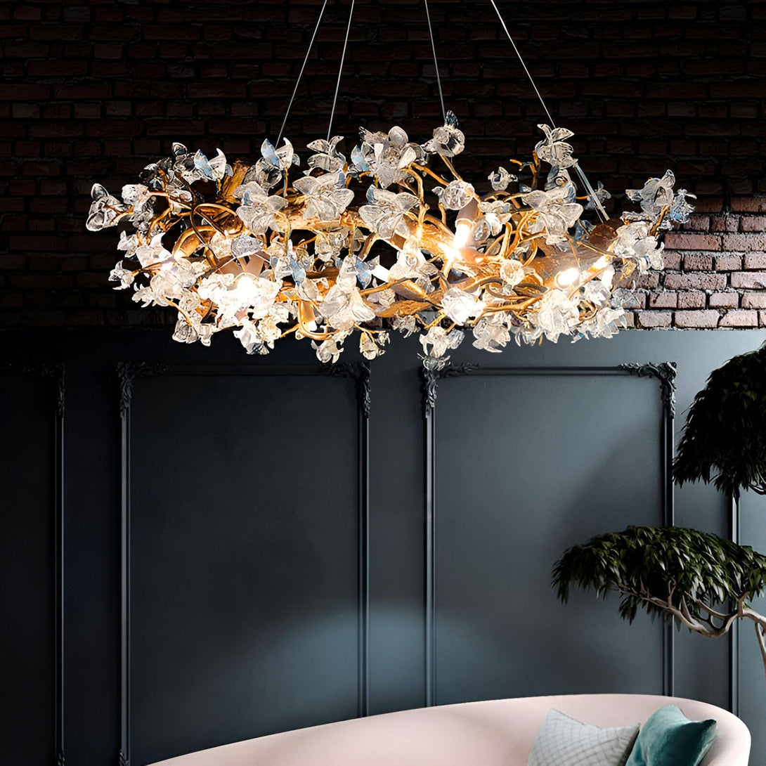 Une image d'un lustre en forme de fleurs en cristal. Le lustre est suspendu au plafond et est éclairé par des lumières LED. Le lustre est composé de plusieurs branches de fleurs en cristal qui sont disposées en cercle. Les fleurs en cristal sont de couleur transparente et sont de différentes tailles. Le lustre est suspendu à l'aide de câbles métalliques qui sont fixés au plafond.