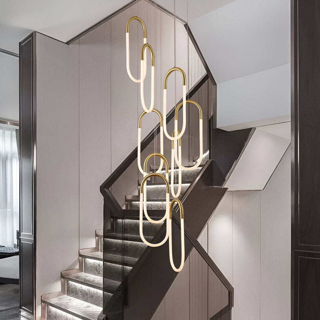 Une image d'un lustre doré suspendu dans une cage d'escalier. Le lustre est composé de plusieurs anneaux de différentes tailles, et il est éclairé par des LED. NA-0096577770,NA-4868161806,NA-0573753911,