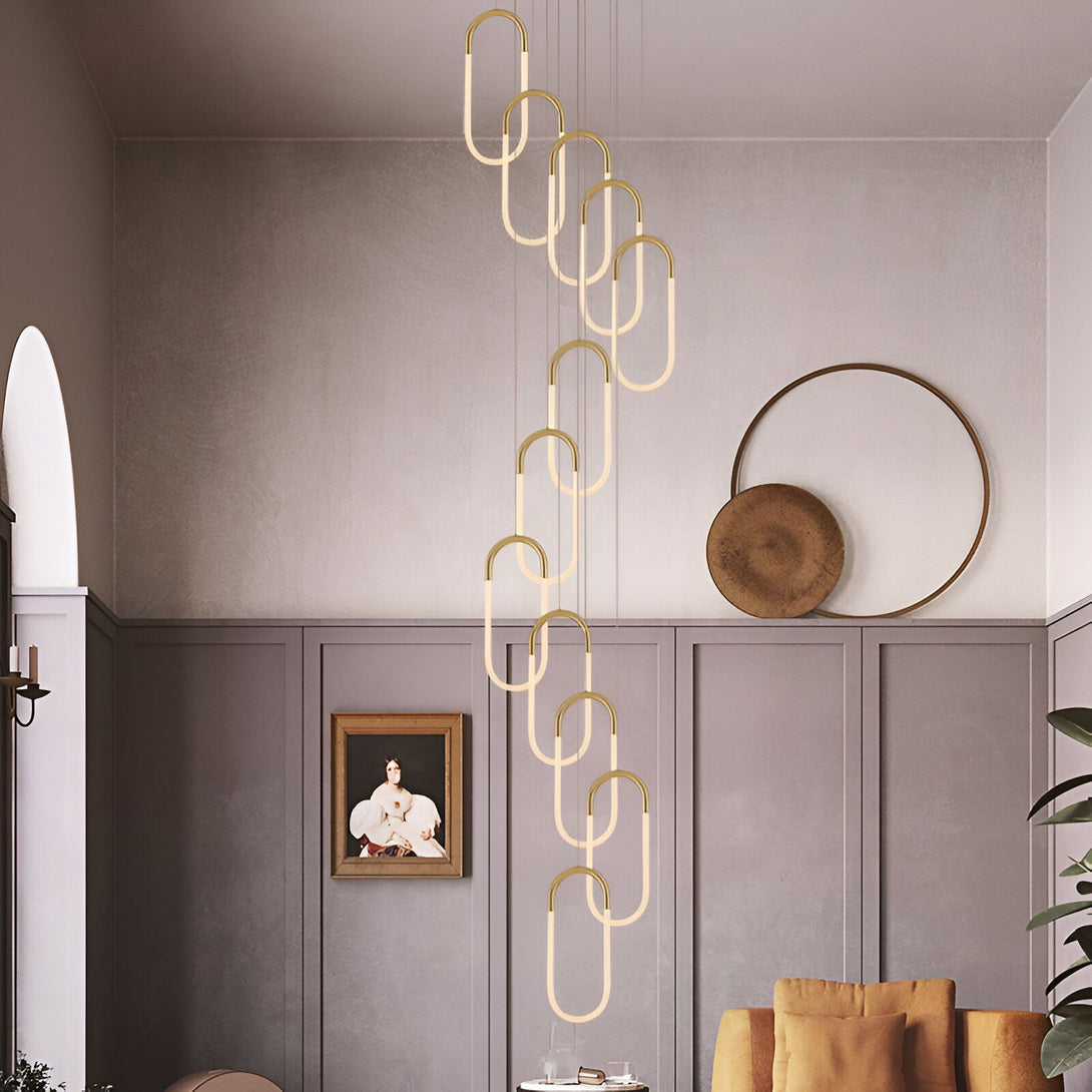 Une image d'un salon avec une suspension lumineuse design en forme d'anneaux ovales en métal doré. Le salon est décoré dans un style moderne avec des murs gris et un canapé marron. NA-0096577770,NA-4868161806,NA-0573753911,