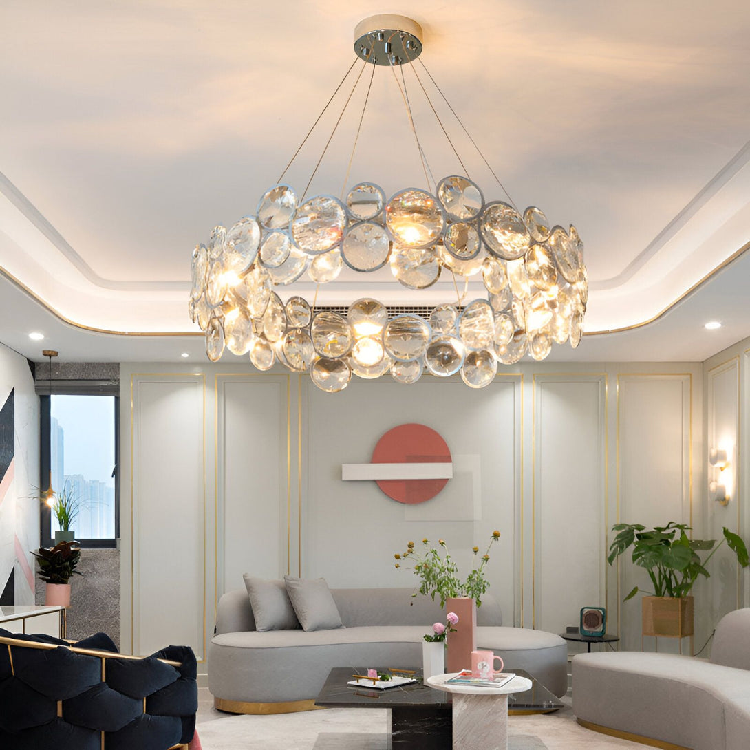 Une image d'un lustre rond en cristal avec des ampoules allumées. Le lustre est suspendu au plafond et il y a un canapé en dessous. Il y a aussi une table basse avec des verres dessus. PE-3049239069,PE-966204308X,PE-4267310149,