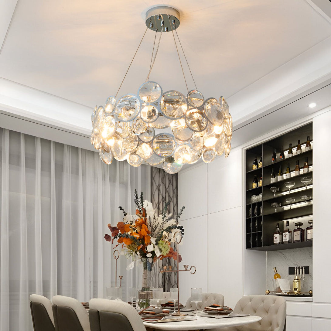 Une image d'un lustre en cristal avec des ampoules allumées. Le lustre est suspendu au plafond et il y a une table en dessous avec des chaises autour. Il y a des fleurs sur la table. PE-3049239069,PE-966204308X,PE-4267310149,