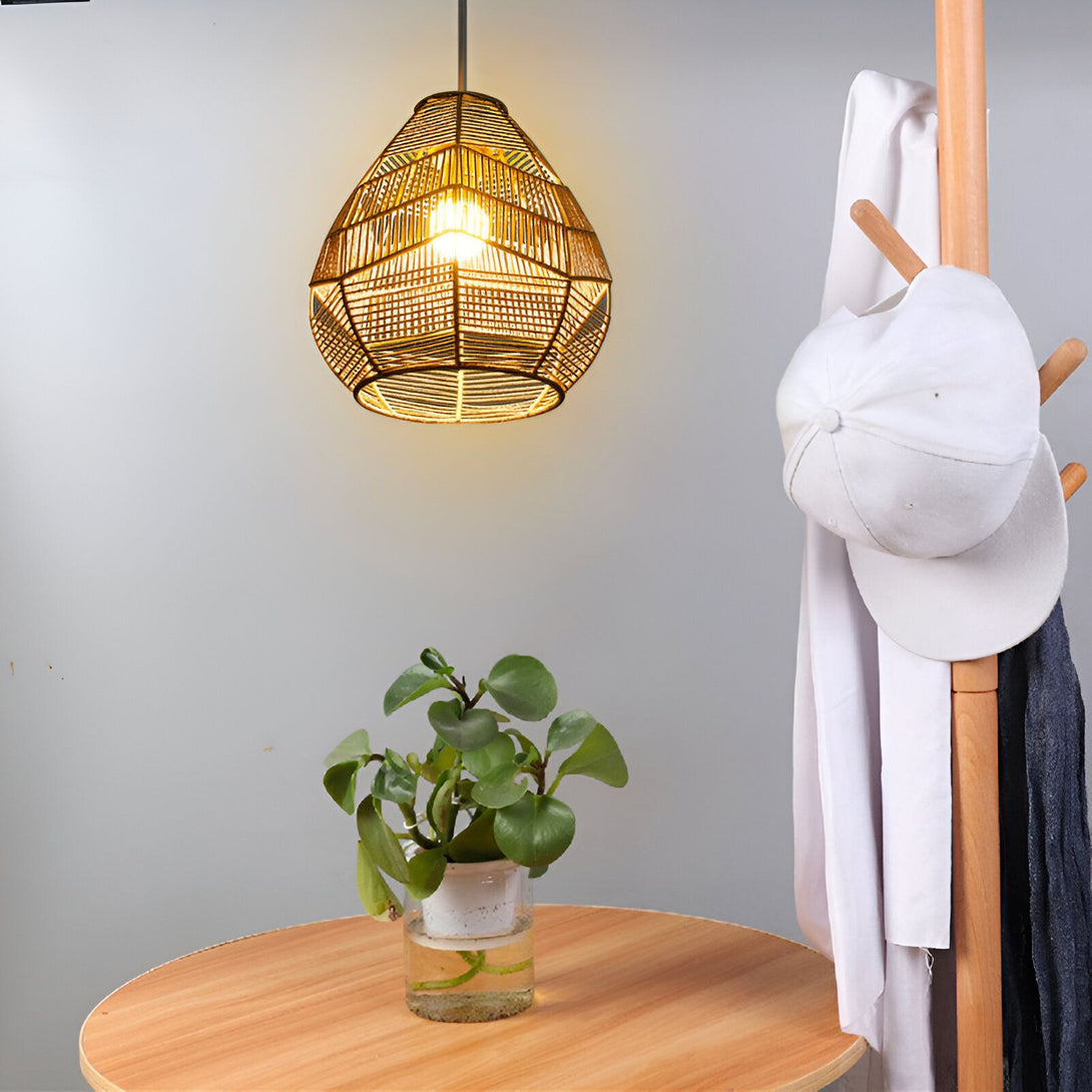 Une lampe en osier suspendue au plafond. À côté, sur une table en bois, se trouve une plante verte dans un vase en verre transparent. Derrière la chaise, on aperçoit un porte-manteau en bois avec un chapeau blanc suspendu. AL-7279960006,
