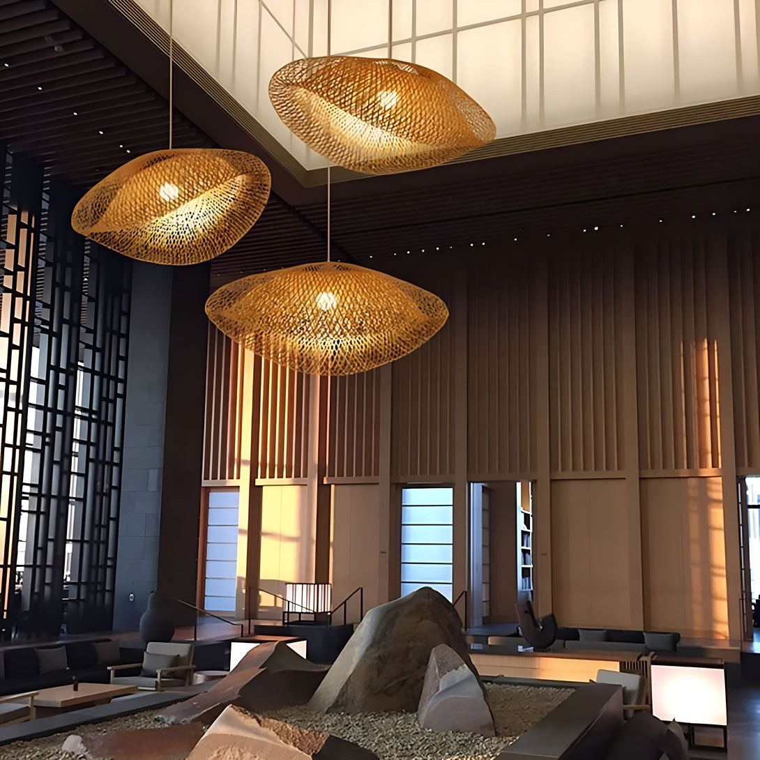 Une image de trois lampes suspendues en bambou tressé main. Les lampes sont de forme ovale et ont une couleur naturelle. Elles sont suspendues à différents niveaux au-dessus d'un sol en pierre avec des chaises et des tables basses. SE-7652193869,SE-5885586357,SE-3059155046,SE-7426962288,