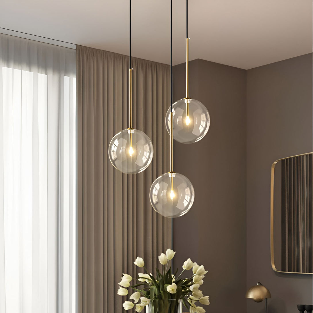 Une image de trois suspensions en verre soufflé avec des ampoules dorées. Les suspensions sont accrochées à des fils noirs et sont de différentes hauteurs.