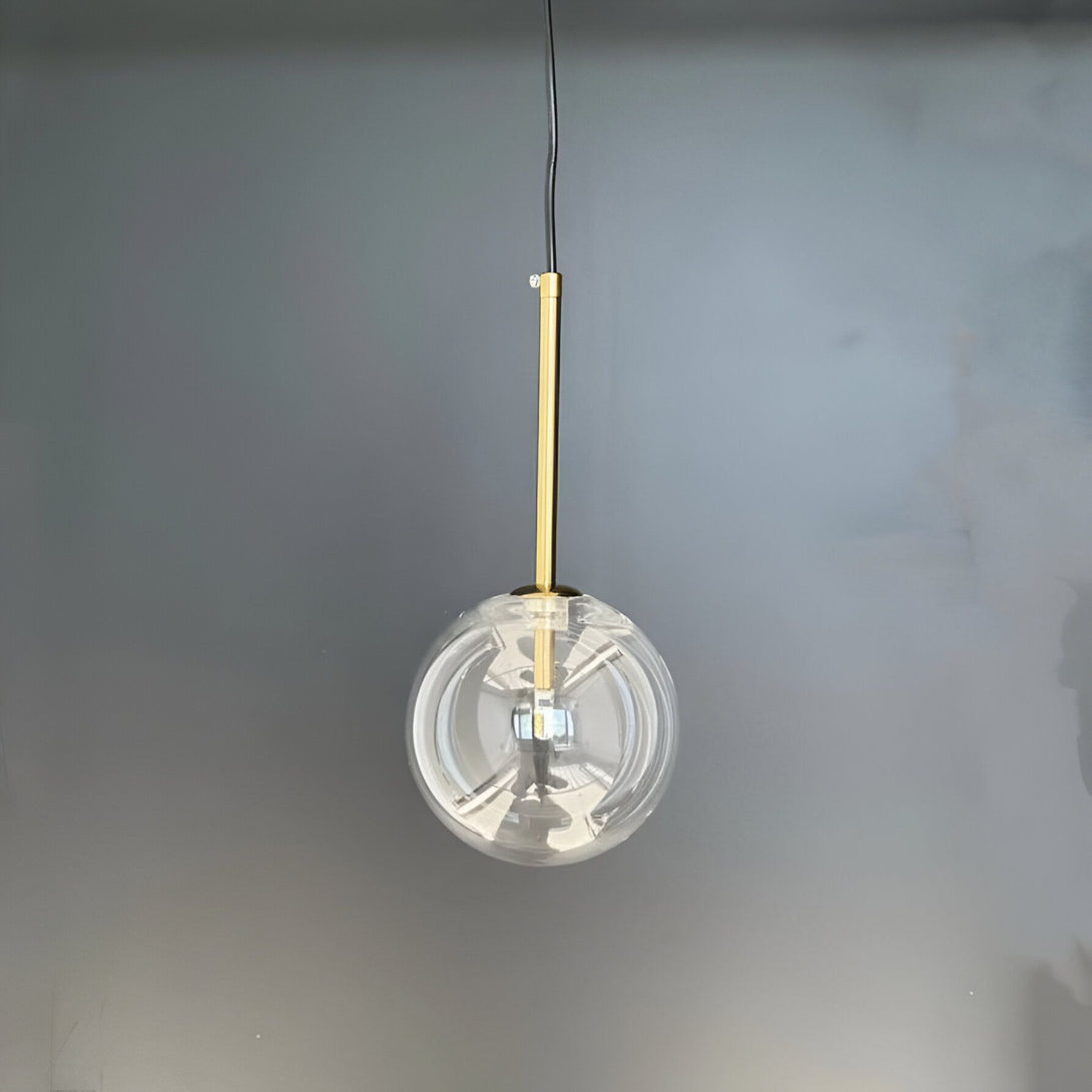 Une image d'une lampe suspendue en verre transparent avec une monture en laiton. La lampe est allumée et émet une lumière douce.
