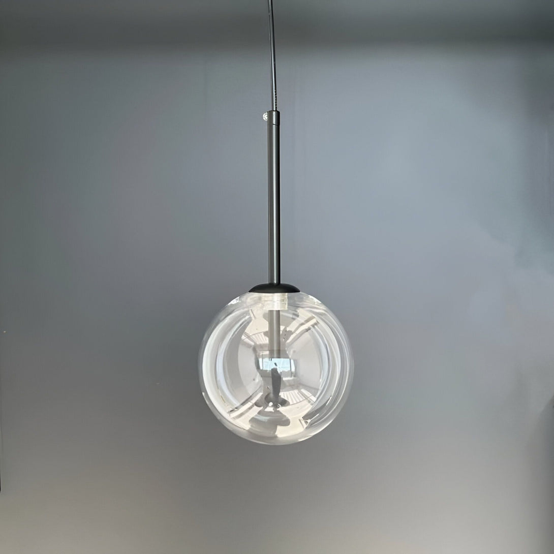 Une image d'une lampe suspendue en verre transparent avec un fil noir. La lampe est allumée et reflète la lumière sur le mur gris.
